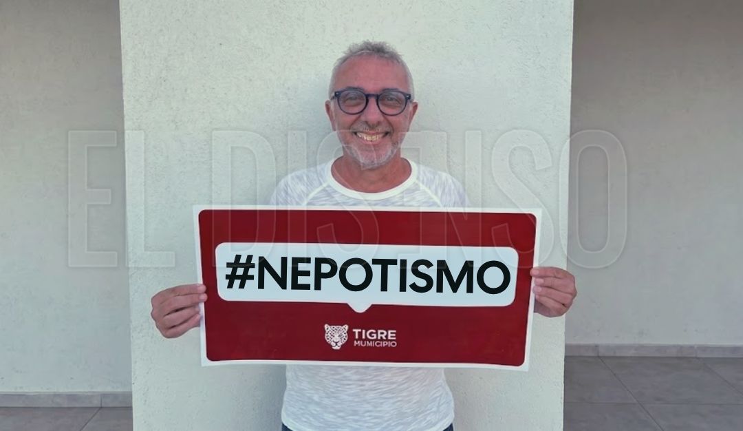 Julio Zamora, intendente de Tigre, posando con un cartel rojo que dice '#NEPOTISMO